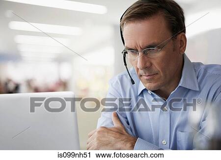 Mature businessman wearing headset and using laptop View Large Photo Image Stock Image - Mature businessman wearing headset and using laptop. Fotosearch