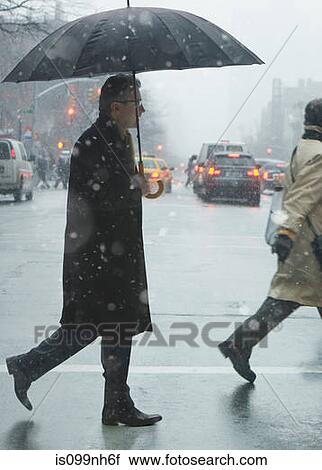 Stock Image - Mature man crossing city street in rain. Fotosearch