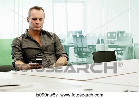 Mature man using cellphone at conference table View Large Photo Image Stock Photo - Mature man using cellphone at conference table. Fotosearch