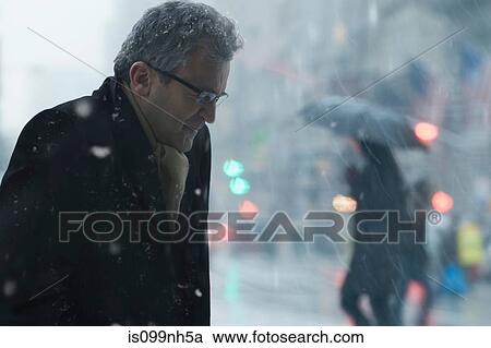 Stock Image - Mature man walking through snowstorm city. Fotosearch