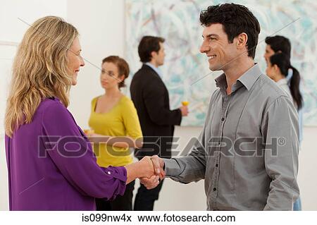 Stock Photo - Mid adult man and woman shaking hands in art gallery. Fotosearch