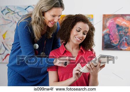 Mid adult woman advising art student drawing in sketch pad in art gallery View Large Photo Image Stock Image - Mid adult woman advising art student drawing in sketch pad in art gallery. Fotosearch