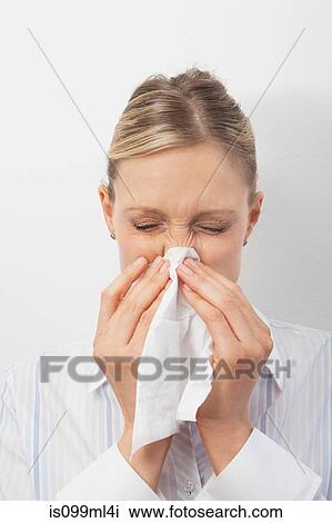 Stock Image - Mid adult woman blowing nose. Fotosearch