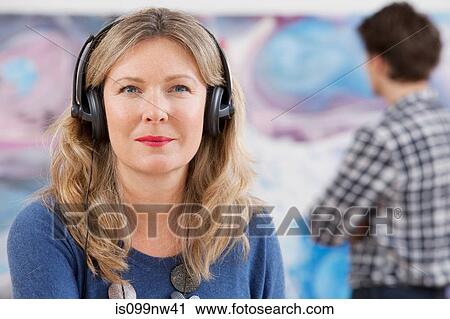 Mid adult woman wearing headphones in gallery View Large Photo Image Stock Image - Mid adult woman wearing headphones in gallery. Fotosearch