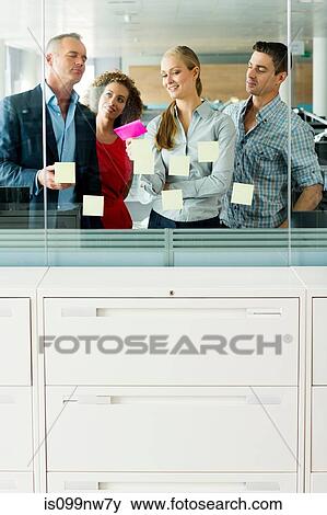 Office colleagues arranging adhesive notes on office window View Large Photo Image Stock Photo - Office colleagues arranging adhesive notes on office window. Fotosearch