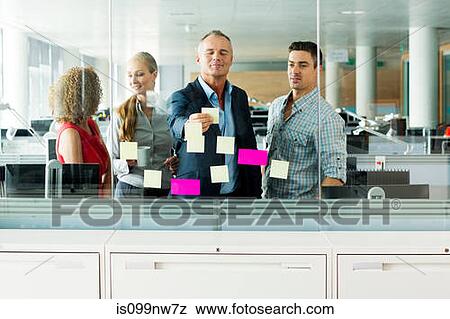 Office colleagues arranging adhesive notes on office window View Large Photo Image Stock Photo - Office colleagues arranging adhesive notes on office window. Fotosearch