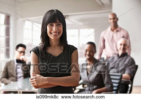 Stock Image - Portrait of businesswoman with colleagues in background. Fotosearch