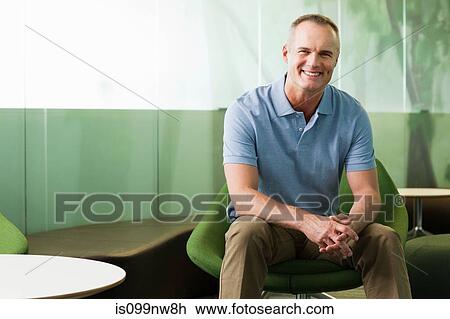 Stock Image - Portrait of mature man sitting in green chair in office. Fotosearch