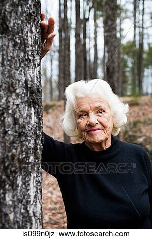 Portrait of senior woman leaning on tree trunk in forest View Large Photo Image Stock Photo - Portrait of senior woman leaning on tree trunk in forest. Fotosearch