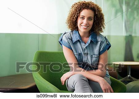 Stock Image - Portrait of young woman sitting in green chair in office. Fotosearch