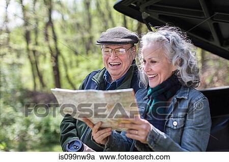 Stock Image - Senior couple reading map while sitting on car trunk in forest. Fotosearch