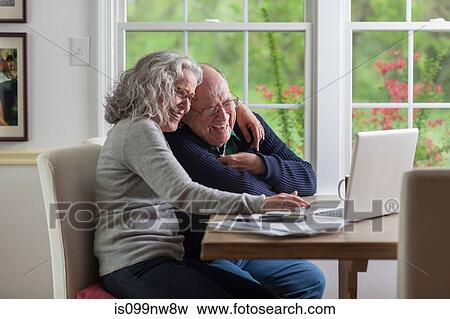 Stock Photo - Senior couple using laptop at home, laughing. Fotosearch
