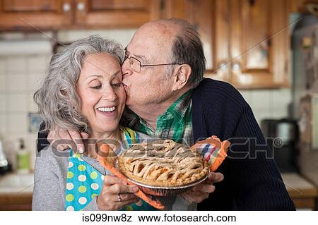 Stock Photo - Senior man kissing woman holding freshly baked pie. Fotosearch