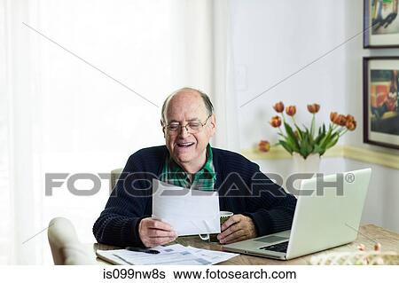 Senior man looking at documents on desk at home View Large Photo Image Stock Photograph - Senior man looking at documents on desk at home. Fotosearch