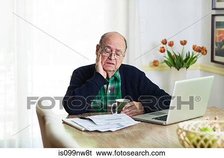 Senior man looking at documents on desk at home View Large Photo Image Stock Photograph - Senior man looking at documents on desk at home. Fotosearch