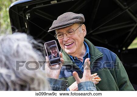 Stock Image - Senior woman taking picture message of smiling man outdoors. Fotosearch