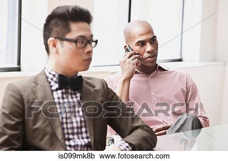 Stock Image - Two businessmen, one on the phone. Fotosearch
