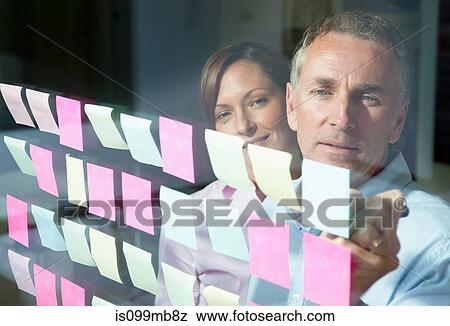 Two businesspeople writing on adhesive notes on window View Large Photo Image Stock Photo - Two businesspeople writing on adhesive notes on window. Fotosearch