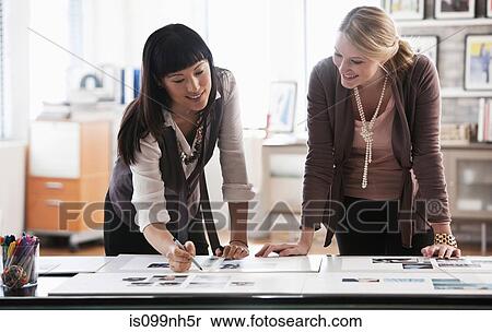 Two creatives studying designs on desk View Large Photo Image Stock Photography - Two creatives studying designs on desk. Fotosearch