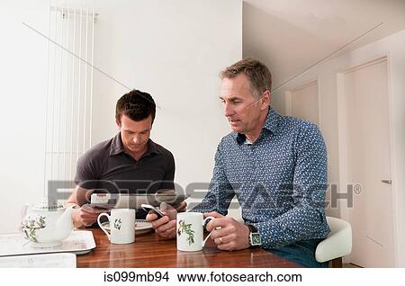 Two men sitting at table with mugs of tea View Large Photo Image Picture - Two men sitting at table with mugs of tea. Fotosearch