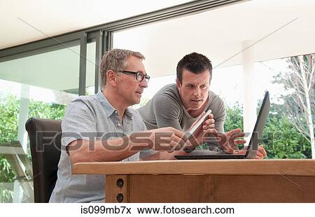 Two men using laptop in home office View Large Photo Image Stock Photo - Two men using laptop in home office. Fotosearch