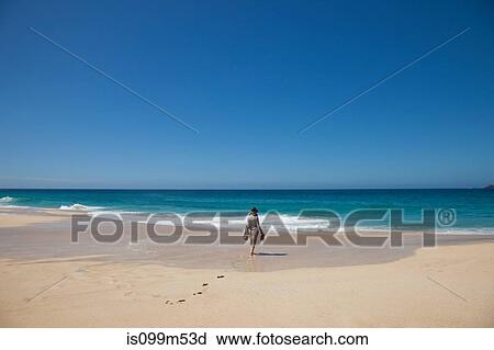 Stock Image - Woman alone on a beach, walking toward the sea. Fotosearch