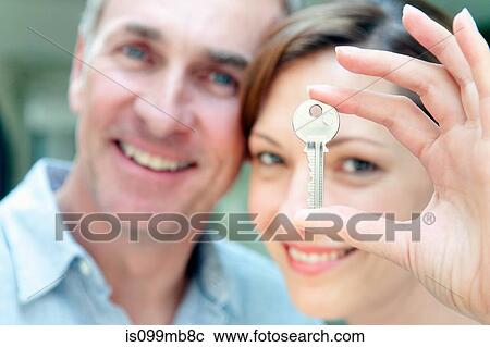 Stock Image - Woman holding house key, man in background. Fotosearch