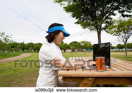 Woman using laptop on picnic bench in the park View Large Photo Image Stock Photography - Woman using laptop on picnic bench in the park. Fotosearch