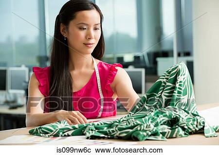 Stock Image - Young fashion designer at desk working with green fabric. Fotosearch
