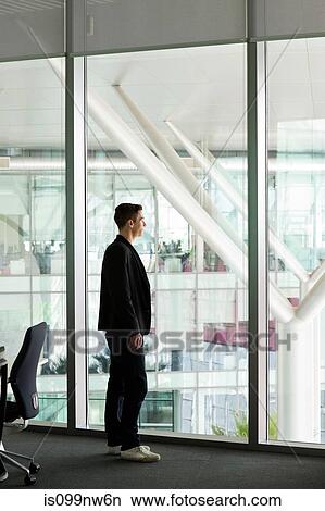 Young man looking out of window in IT office View Large Photo Image Picture - Young man looking out of window in IT office. Fotosearch