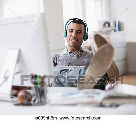 Young man relaxing at desk in office View Large Photo Image Picture - Young man relaxing at desk in office. Fotosearch