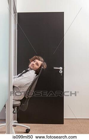 Stock Image - Young man sitting in office doorway. Fotosearch