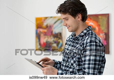 Stock Photo - Young man using digital tablet in art gallery. Fotosearch