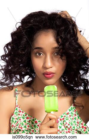 Picture - Young woman eating green popsicle, portrait. Fotosearch