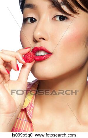 Stock Image - Young woman eating raspberry, portrait. Fotosearch