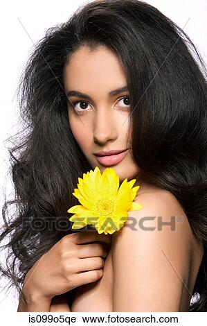 Stock Image - Young woman holding yellow flower against white background. Fotosearch