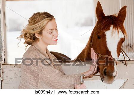 Stock Image - Young woman looking after horse in stable. Fotosearch