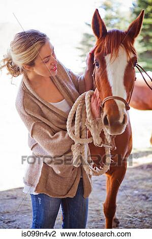 Stock Image - Young woman looking after horse on farm. Fotosearch