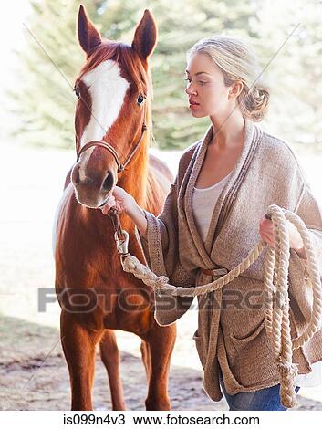 Young woman looking after horse on farm View Large Photo Image Stock Image - Young woman looking after horse on farm. Fotosearch