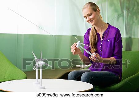 Stock Image - Young woman looking at model of wind turbine. Fotosearch