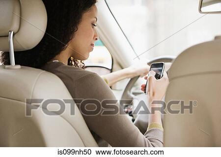 Stock Image - Young woman text messaging on cellphone from car. Fotosearch
