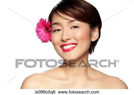 Stock Photograph - Young woman wearing pink flower in hair against white background. Fotosearch