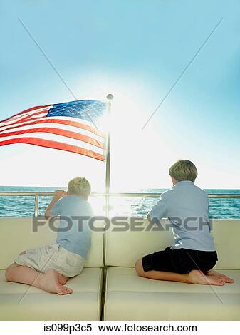 Stock Photography - Boys in the back of a yacht with american flag, looking out to sea. Fotosearch