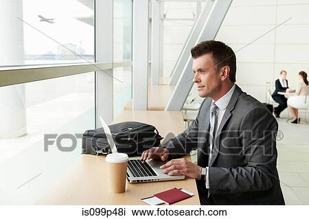 Stock Image - Businessman using laptop in airport. Fotosearch