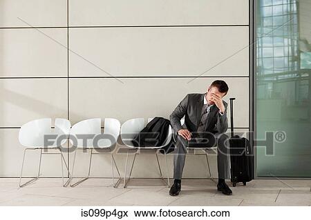 Stock Photo - Businessman waiting with luggage and head in hands. Fotosearch