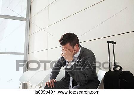 Stock Photo - Businessman waiting with luggage, head in hands. Fotosearch