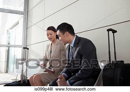 Stock Image - Businesspeople with digital tablet and luggage. Fotosearch
