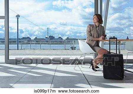 Picture - Businesswoman sitting in airport with suitcase. Fotosearch