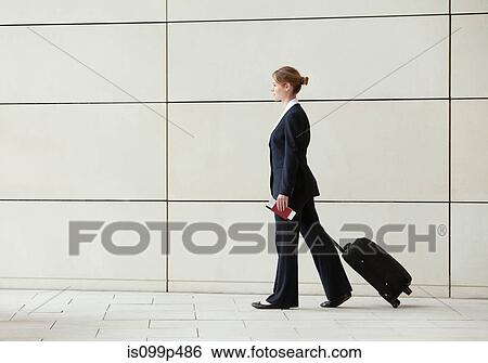 Stock Photograph - Businesswoman walking pulling luggage. Fotosearch