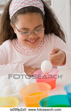 Stock Image - Girl coloring an egg for easter. Fotosearch